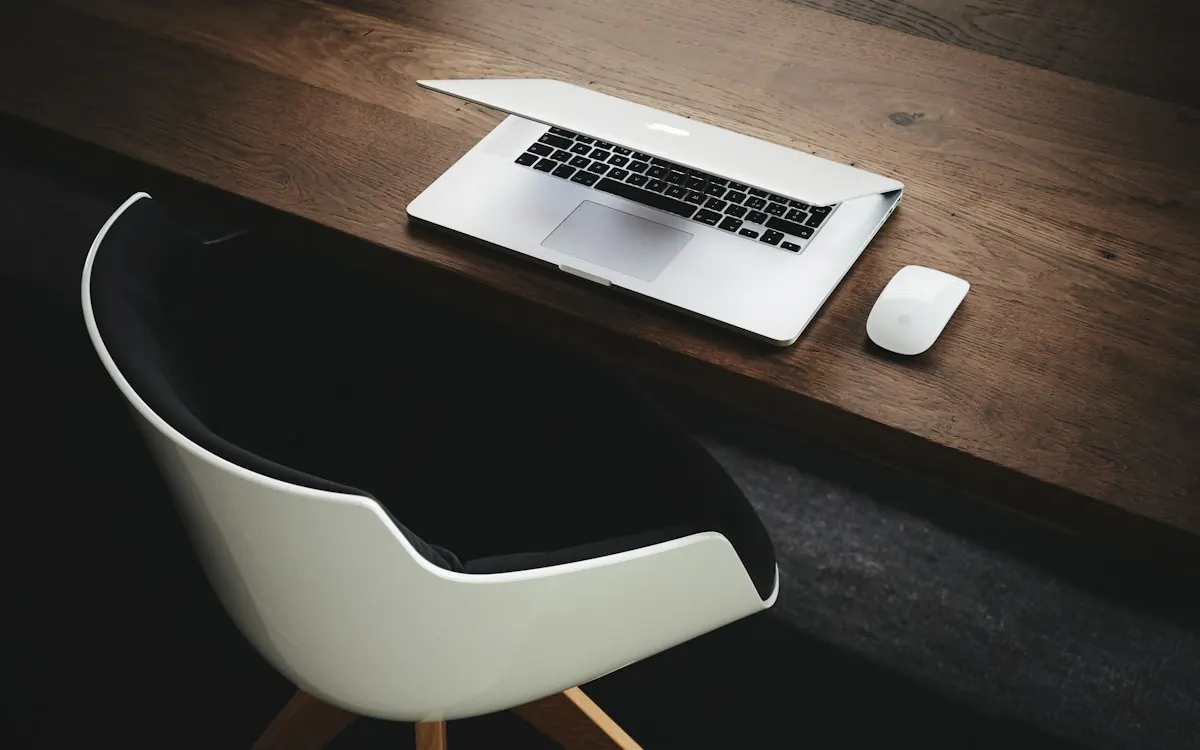 Laptop and mouse on a dark wooden desk beside a white office chair